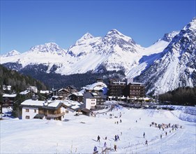 Arosa, Plessur, Switzerland. Ski resort with people skiing in the foreground and the Alps behind.