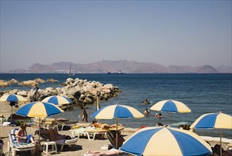 Kos, Dodecanese Islands, Greece. Tigaki Beach. Sunbathers on loungers with blue and yellow striped