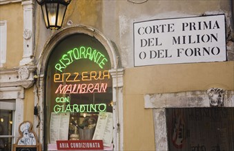 Venice, Veneto, Italy. Centro Storico Pizzeria window in old city wall with neon advertising menus