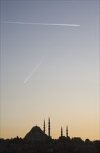 Istanbul, Turkey. Sultanahmet. Suleymaniye Mosque silhouetted against pale sunset sky with aircraft