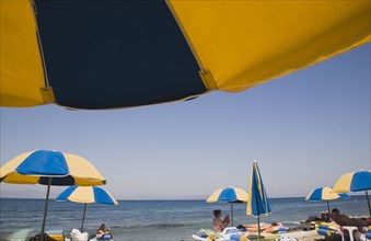 Kos, Dodecanese Islands, Greece. Sunbathers on loungers underneath yellow and blue striped beach