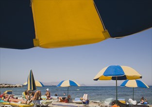 Kos, Dodecanese Islands, Greece. Sunbathers on loungers and blue and yellow striped beach parasols