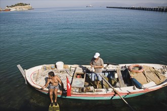 Kusadasi, Aydin Province, Turkey. Local fisherman in fishing boat with family member preparing to