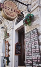 Budapest, Pest County, Hungary. Bazilika Cafe and Restaurant exterior with hanging sign and menu
