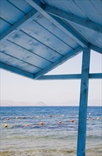 Kos, Dodecanese, Greece. View over red and yellow floats in water part framed by roof of blue