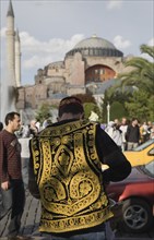 Istanbul, Turkey. Sultanahmet Man wearing embroidered waistcoat and cap standing at food stall in