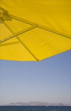 Kos, Dodecanese Islands, Greece. Underside of bright yellow sun umbrella framing view across sea to
