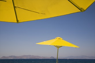 Kos, Dodecanese Islands, Greece. Bright yellow parasols on beach outside Kos Town with view towards