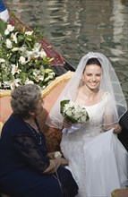 Venice, Veneto, Italy. Smiling bride in wedding dress and veil carrying bouquet of white roses