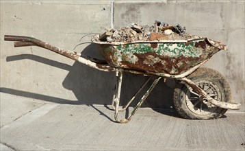 Rusting wheelbarrow with a flat tyre against newly laid concrete. Industry Construction Building