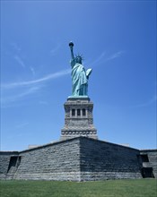 New York, New York State, USA. Statue of Liberty. Green statue with gold torch flame stone wall and