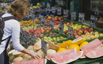 Vienna, Austria. The Naschmarkt. Female customer selecting melon from display on market fruit stall