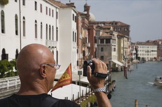 Venice, Veneto, Italy. Male tourist making a video recording from bridge looking along canal in