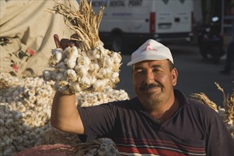 Kusadasi, Aydin Province, Turkey. Stallholder at weekly market holding up bunch of garlic bulbs