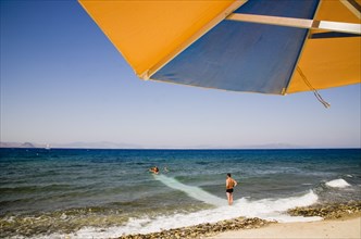 Kos, Dodecanese Islands, Greece. Holidaymakers on beach outside Kos Town with blue and orange