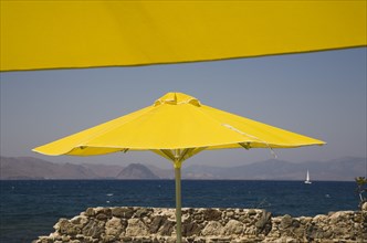 Kos, Dodecanese Islands, Greece. Bright yellow parasols on beach outside Kos Town with crumbling