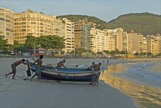 Rio de Janeiro, Brazil. Launching a fishing boat at Copacabana beach at daybreak fishermen and a