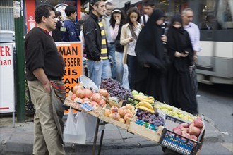 Istanbul, Turkey. Sultanahmet. Two women wearing burqa and veil passing fresh fruit stall with male
