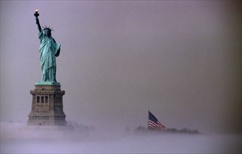 Liberty Island, New York, USA. Statue of Liberty and Stars and Stripes Flag on misty morning. USA