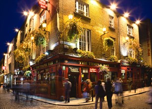 Ireland, County Dublin, Dublin City, Temple Bar Pub illuminated at night with people walking past
