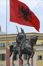 Albania, Tirane, Tirana, National flag depicting two headed eagle flying above equestrian statue of