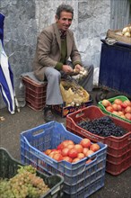 Albania, Tirane, Tirana, Fruit and vegetable street vendor in the Avni Rustemi Market seated on