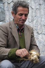 Albania, Tirane, Tirana, Portrait of a male street vendor bunching bulbs of garlic together for