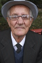 Albania, Berat, Head and shoulders portrait of an elderly man wearing hat and glasses  looking