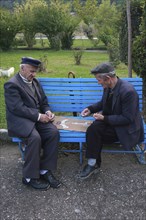Albania, Berat, Two elderly men playing dominos on park bench.