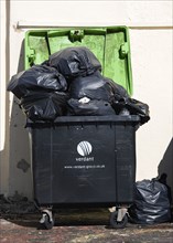 England, West Sussex, Bognor Regis, Wheeled waste bin container overflowing with full large black
