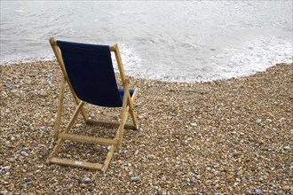 England, West Sussex, Bognor Regis, Single dark blue deck chair on pebble shingle beach looking out