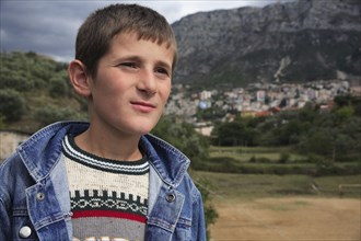 Albania, Kruja, Head and shoulders portrait of a teenage boy with the town of Kruja in the