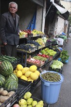 Albania, Tirane, Tirana, Grocer beside his shop front display of fruit and vegetables including