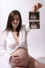 Health, Pregnancy, Scan, Young  pregnant woman holding up her ultrasound scan photograph with one