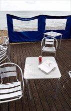 England, West Sussex, Bognor Regis, Empty aluminium chairs and tables on wooden decking behind a