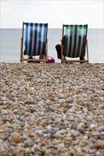 England, West Sussex, Bognor Regis, Two elderly seniors sitting on deck chairs on the pebble