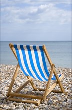 England, West Sussex, Bognor Regis, Single blue and white deck chair on the shingle pebble beach
