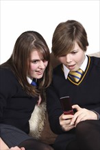 Children, Teenagers, Girls, Teenage girls in school uniform texting on a mobile phone.