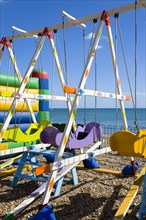 England, West Sussex, Bognor Regis, Colourful amusement swings on the pebble shingle beach by the