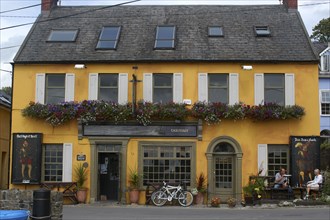 Ireland, Cork, Kinsale, Public House yellow facade with couple sitting outside