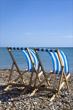 England, West Sussex, Bognor Regis, Two blue and white deck chair on the shingle pebble beach