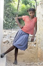 Haiti, La Gonave, Young happy smiling girl leant against the wall of a slum building.