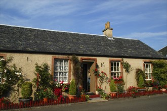 Scotland, Argyll and Bute, Luss, Cottage with flowers and pot plants outside and an open doorway