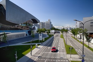 BMW Welt showroom on left hand side opposite the head-quarters building with car on multi-lane road