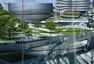 BMW Headquarters and museum reflected in glass facade of BMW Welt showroom creating distorted image