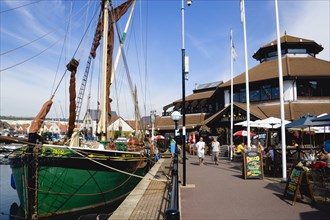 Port Solent Sailing barge SB Kitty moored in the marina with people walking past a pub and