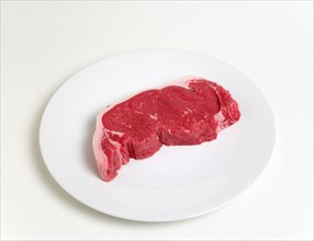 Slice of raw uncooked sirloin steak on a round white plate against a white background. Photo: Paul