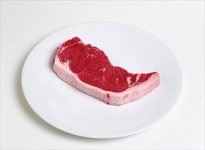 Slice of raw uncooked sirloin steak on a round white plate against a white background. Photo : Paul