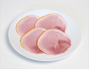 Slices of cured ham on a round white plate on a white background. Photo : Paul Seheult