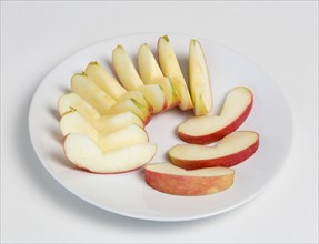 Slices of ripe apple on a white plate against white background. Photo : Paul Seheult